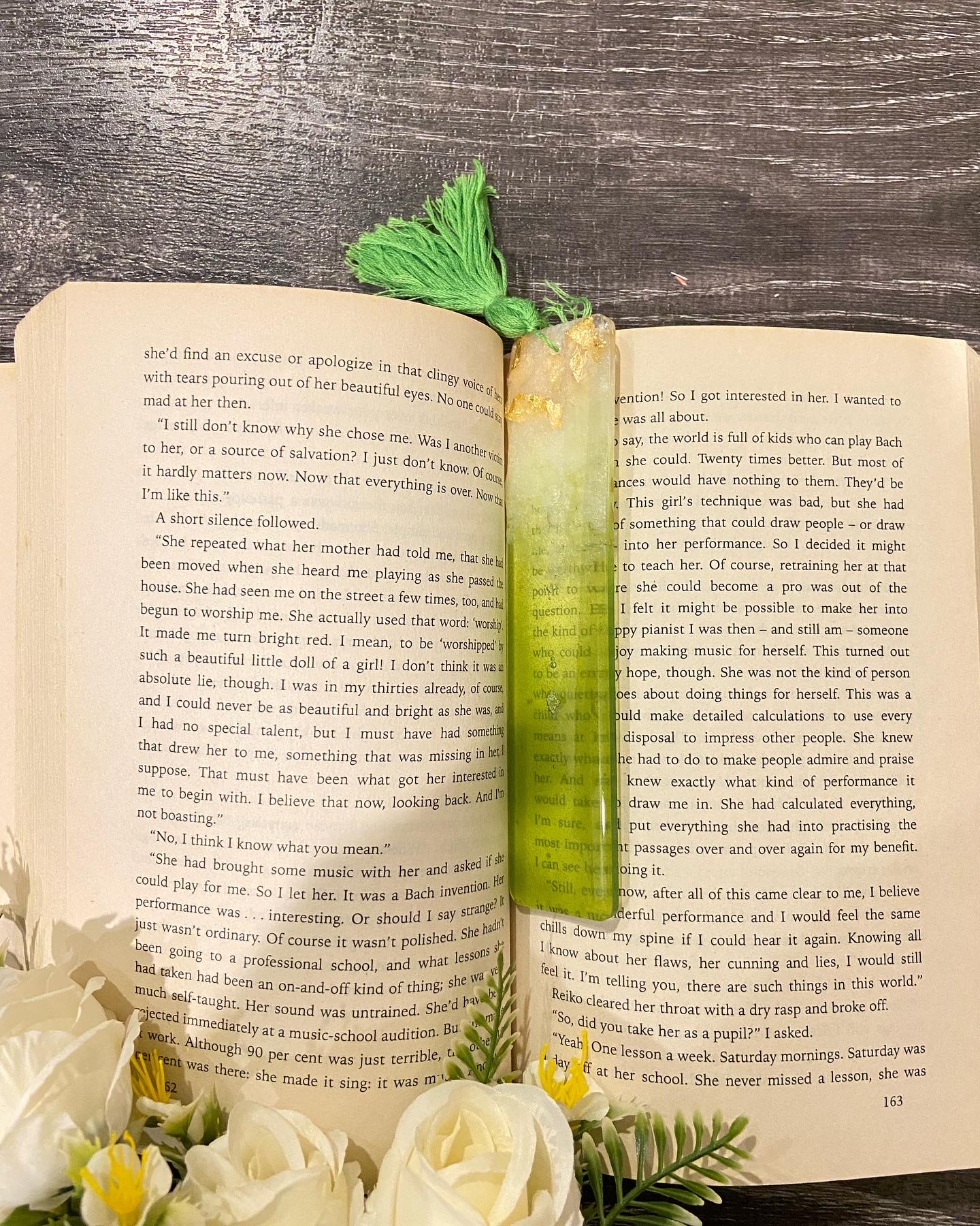 Green resin bookmark with gold flakes and a green tassel on an open book