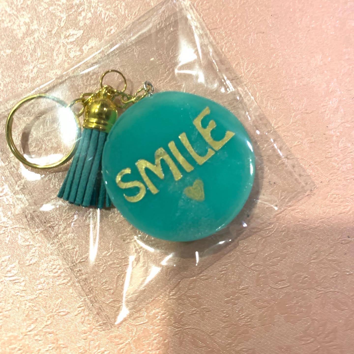 Teal smile keychain with gold lettering and matching tassel