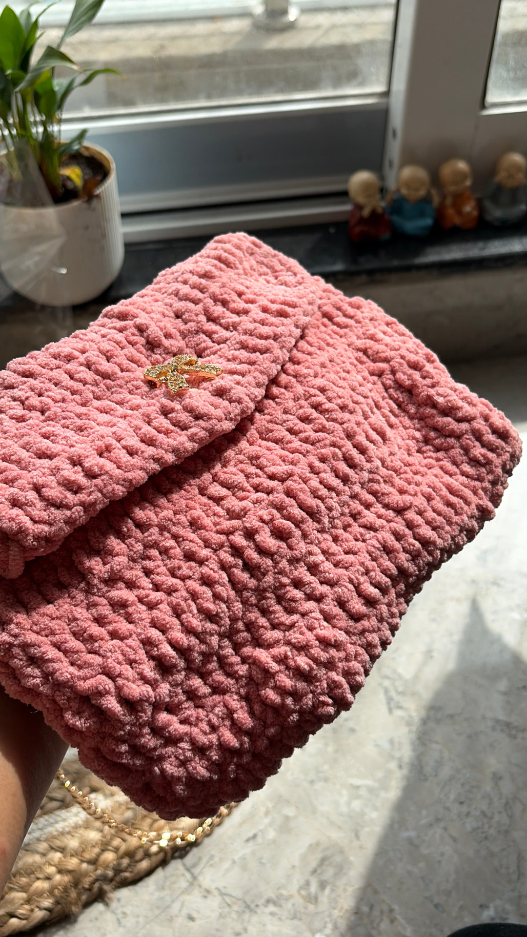 Rose pink chenille crochet clutch bag with gold bow charm held in sunlight