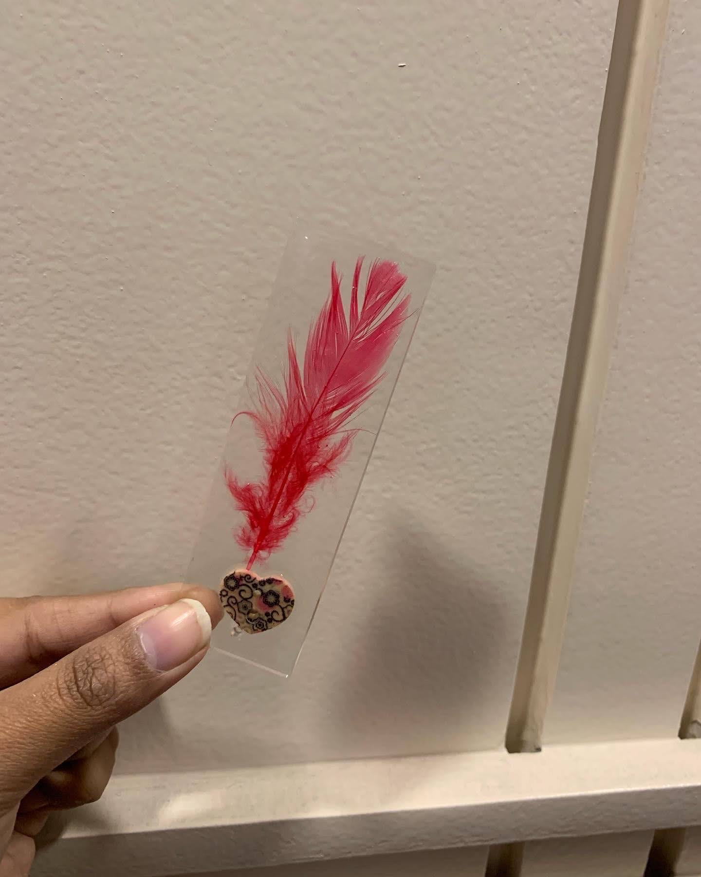Clear resin bookmark with a red feather and tiny painted heart charm