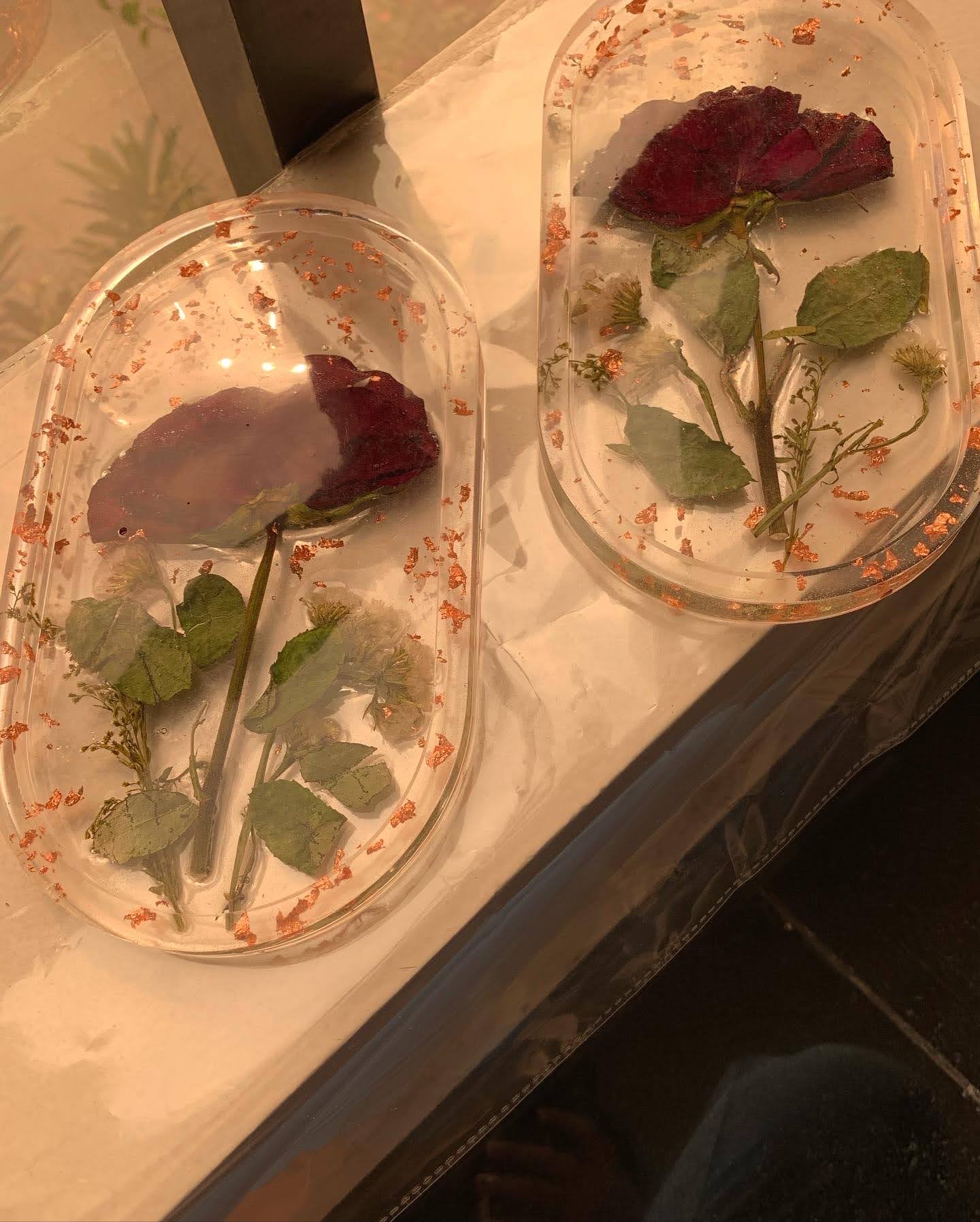 Two oval resin trays preserving pressed roses, leaves and copper flakes