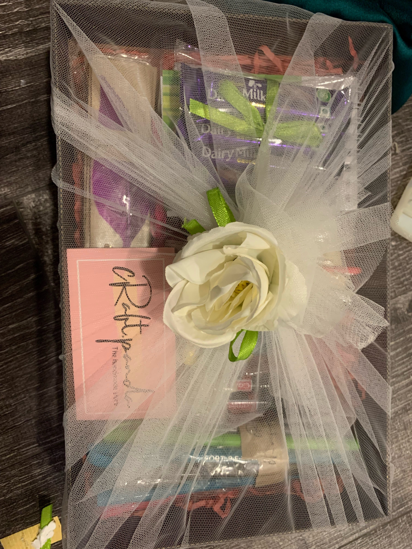 Long pastel hamper of chocolates wrapped in ivory tulle with a white rose