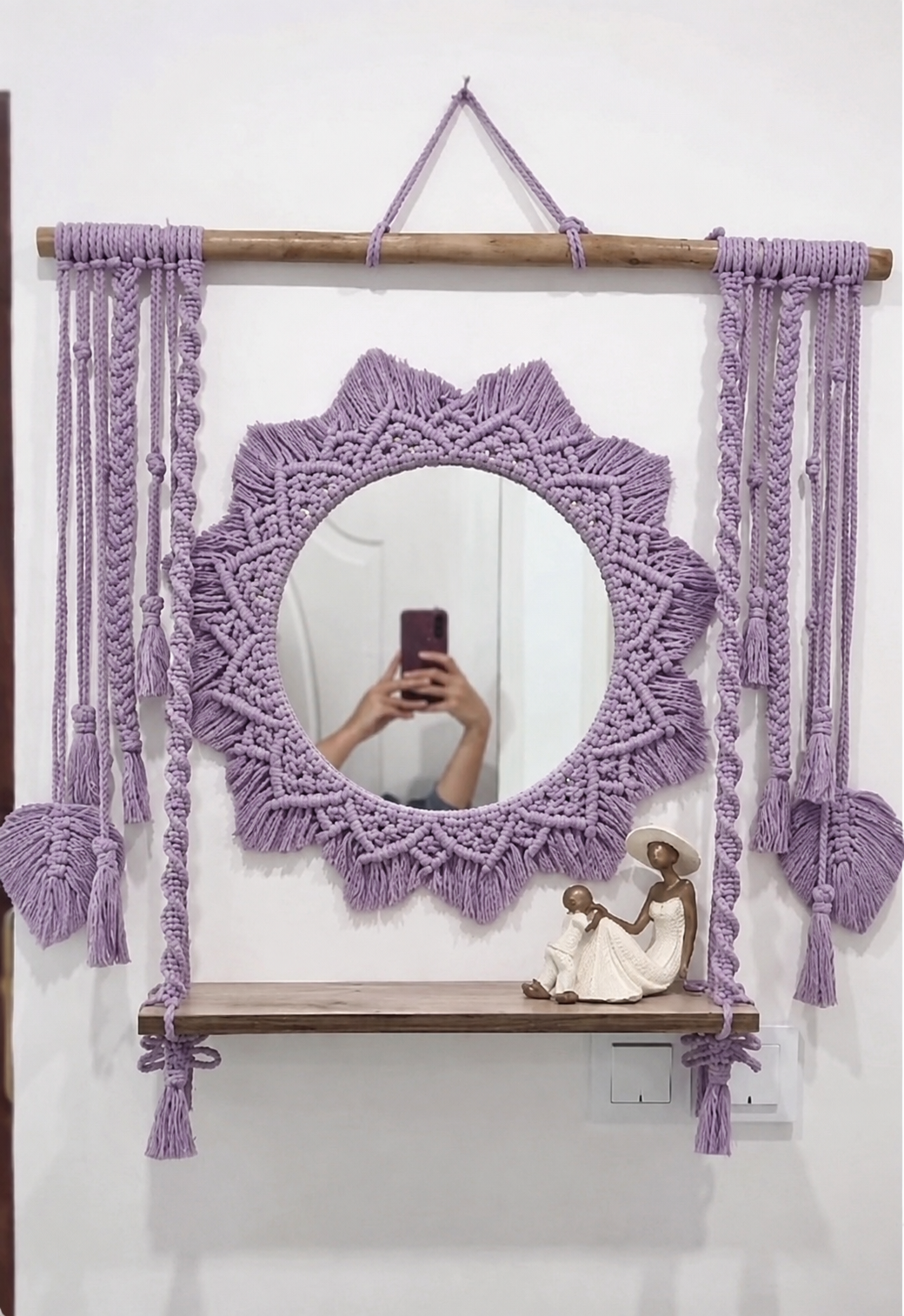Lavender macramé mandala mirror with wooden shelf and tassels on a white wall